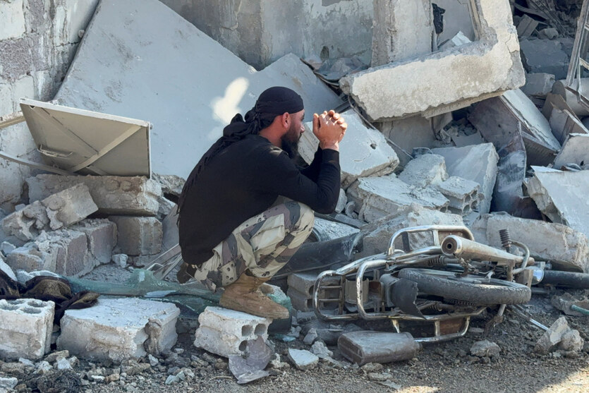Ein junger Mann hockt zwiscchen den Trümmern eines Hauses, vor ihm liegt ein zerstörtes Moped