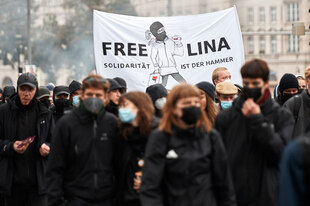 Eine Gruppe von schwarz gekleideten und vermummten DemonstrantInnen (Corona) hält ein Transparent in die Höhe auf dem Freiheit für Lina E. gefordert wird und 