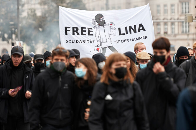 Eine Gruppe von schwarz gekleideten und vermummten DemonstrantInnen (Corona) hält ein Transparent in die Höhe, auf dem Freiheit für Lina E. gefordert wird und "Solidarität ist der Hammer"