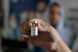 Eine Hand hält eine kleine Flasche mit Impfstoff in die Kamera