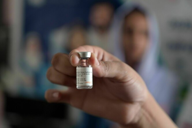 Eine Hand hält eine kleine Flasche mit Impfstoff in die Kamera