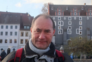 Ein älterer Mann blickt vor Altstadthäusern in herbstlicher Wetterstimmung.