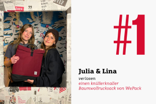 Lina Kurhmann und Julia Molin stehen in der geöffneten, ersten Tür des Adventskalenders und zeigen den Rucksack, den man bei der Verlosung gewinnen kann