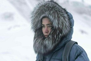 Eine junge Frau steht in einem Schneesturm und trägt eine dicke Pelzjacke