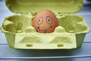 Ein mit einem Smiley bemaltes einzelnes Ei in einem Eierkarton