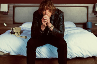 Daniel Avery sitzt auf einem Hotelbett, den Kopf auf die Hände gestützt