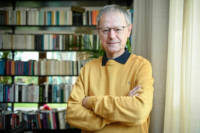 Ein Mann mit gelben Pullover steht vor einem Buchregal