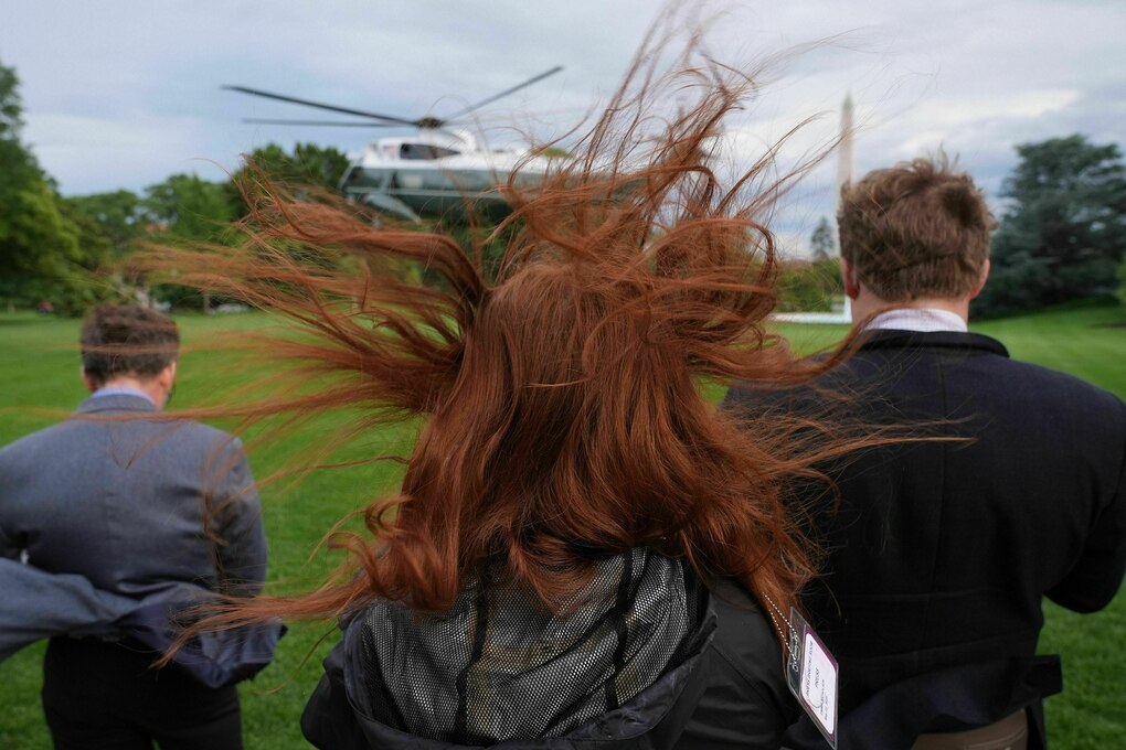 Drei Leute beobachten den Start eines US-amerikanischen Regierungshubschraubers, der Wind der Rotoren wirbelt Haare und Kleidung auf