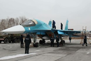 Ein Kampfjet mit mehreren Personen auf einem Flugplatz.