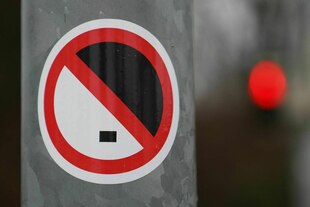 Das Foto zeigt den an einer Ampel angebrachten Aufkleber mit einer stilisierten Adolf Hitler Grafik mit Seitenscheitel und Hitlerbart, die durchgestrichen ist