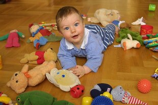 Ein Kleinkind krabbelt auf dem Boden, um es herum sind viele Spielzeuge verteilt