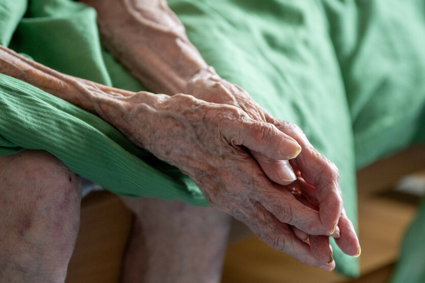 Eine Seniorin sitzt auf ihrem Bett im Altenheim