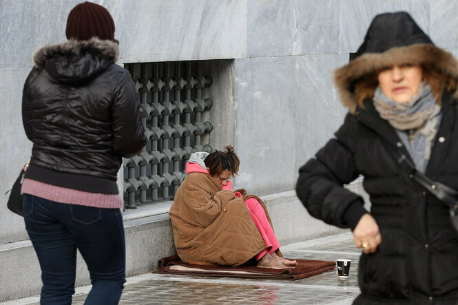 Eine junge Frau bettelt auf der Straße, zwei Passantinnen gehen vorbei