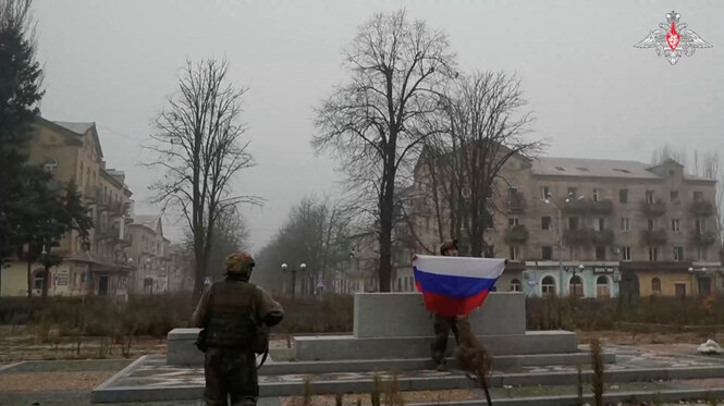 Ein Bild zeigt Soldaten, die in einer Stadt eine russische Flagge hochhalten.
