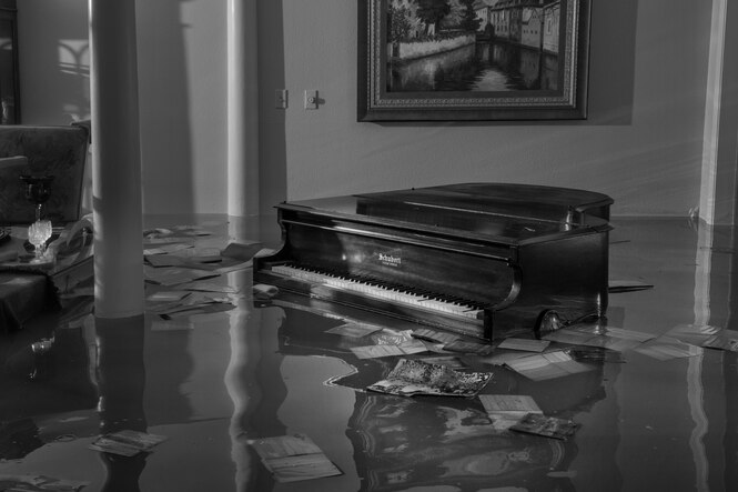 Schwarz-Weiß-Aufnahme von einem überschwemmten herrschaftlichen Wohnzimmer, ein Flügel steht im Wasser