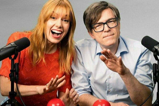 Eine Frau mit roten Haaren und ein Mann sitzen vor zwei Mikrofonen