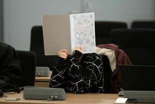 Eine Person versteckt das Gesicht hinter einem aufgeschlagenen Schreibheft