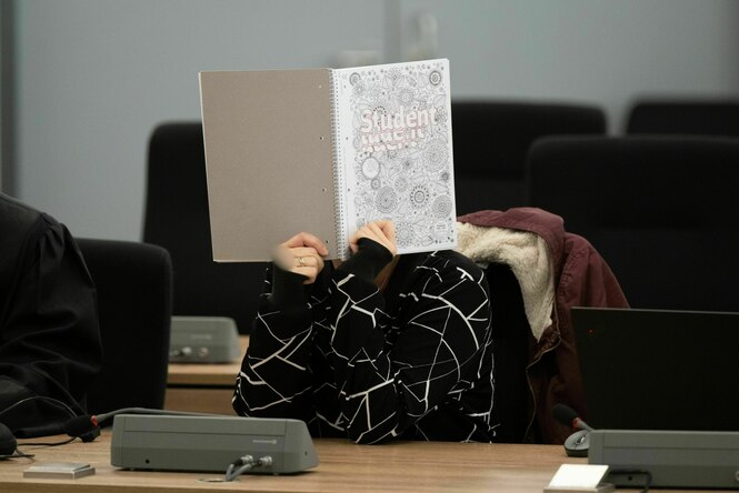 Eine Person versteckt das Gesicht hinter einem aufgeschlagenen Schreibheft