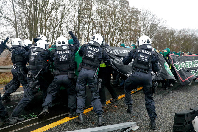 Polizisten prügeln auf Demonstranten ein, die sich hinter einem Banner verstecken