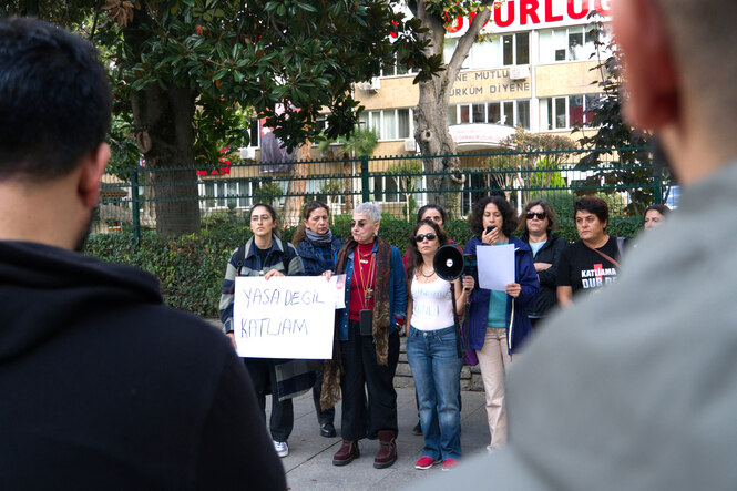 eine Gruppe von Frauen steht auf einem Gehweg - eine Frau hält ein Megafon in der Hand, die andere ein Plakat in der mit der Aufschrift: Kein Gesetz, sondern ein Massker