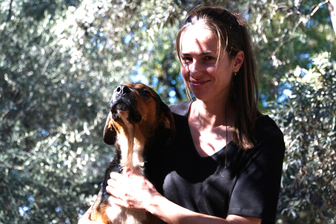 Eine junge Frau mit langen braunen Haaren hält einen Hund im Arm