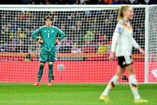 Torhüterin Ann-Katrin Berger stemmt im Hintergrund die Hände in die Hüfte, vor ihr ist unscharf eine Mitspielerin zu sehen