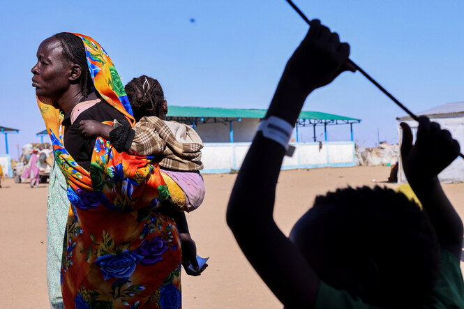 eine Frau in bunten Gewändern trägt ein Baby auf ihrem Rücken