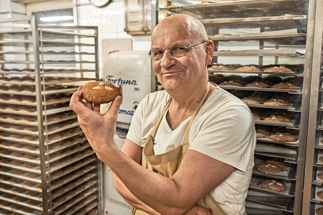Der Bäcker Arnd Erbel hält einen Lebkuchen in der Hand und schaut zufrieden lächelnd in die Kamera