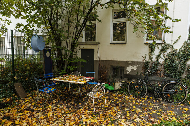 In einem Berliner Hinterhof sind ein Gartentisch und Stühle aufgestellt, alles ist mit herbstlaub bedeckt