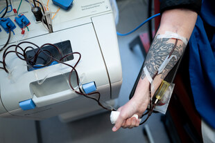 Ein tätowierter Arm mit einer Spritze in der Armbeuge: Eine Frau spendet Blut