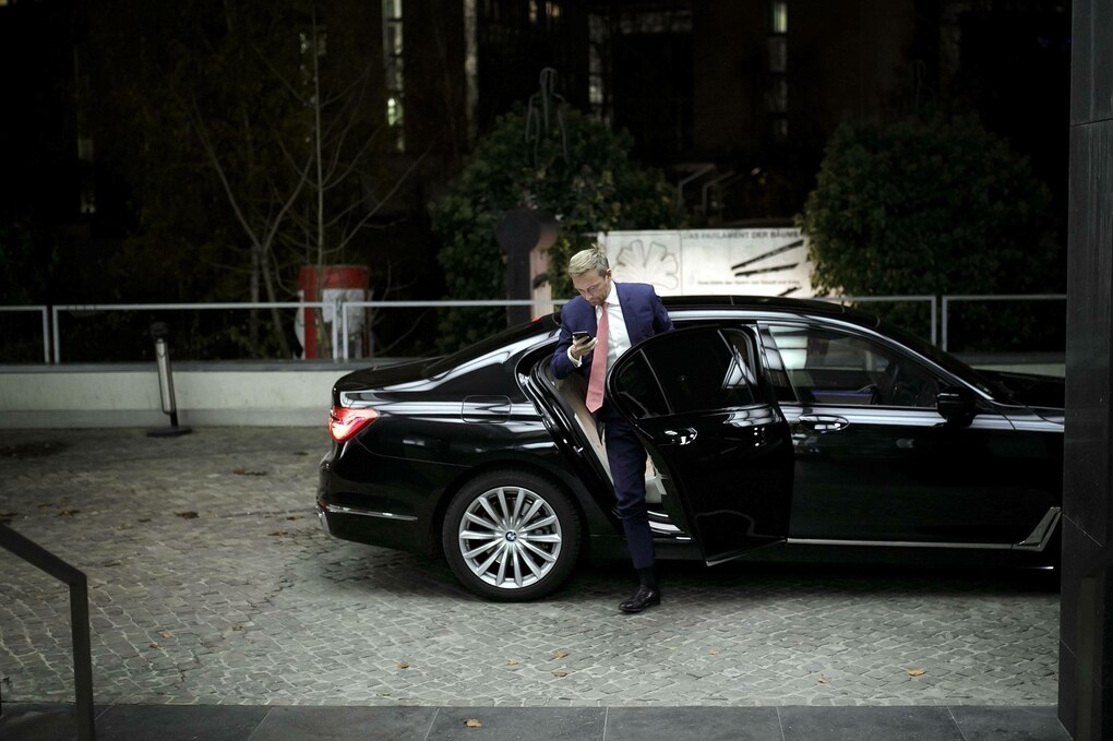 Christian Lindner steigt aus einem schwarzen Auto und schaut auf sein Smartphone, es ist Nacht