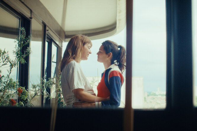 Ella Rumpf und Nadia Monia Chokri sind durch ein Fenster auf einem Balkon zu sehen, wo sie sich umarmen.