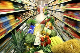 Einkaufswagen gefüllt mit Obst, Gemüse und anderen Lebensmitteln unterwegs zwischen Supermarkt-Regalen