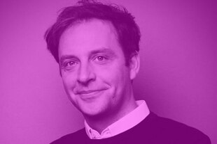 Porträt von Nils Kumkar in weißem Hemd und dunklem Pullover. Sein Blick wirkt ruhig und zugewandt.