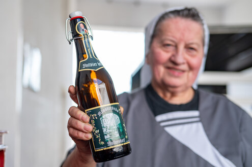 Eine Nonne hält eine Flasche Bier in die Kamera