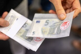 5-Euro-Scheine mit einem roten Aufkleber (Aufschrift: "Donorsday") in den Händen einer Person.