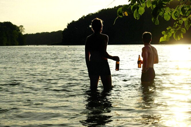 Silhouette von zwei Männern in Badehosen in einem See im Gegenlicht