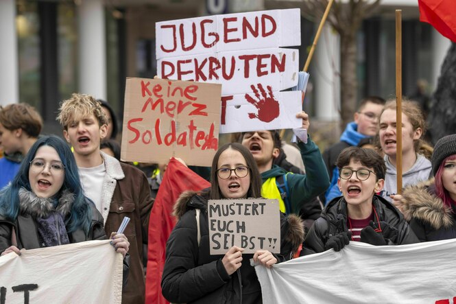 Mehrere Jugendliche bei einer Demonstration. Sie halten Transparente und Schilder in die Luft oder vor sich. Sie haben die Münder geöffnet und rufen etwas.