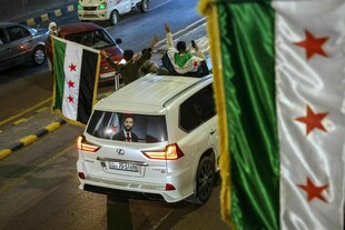 Siegesfeier - Autokonvoy - aus einem hellen Pickup lehnen sich junge Männer, die syrische Flaggen schwenken. An der Heckscheibe ist das Porträt des amtierenden Präsidenten zu sehen.