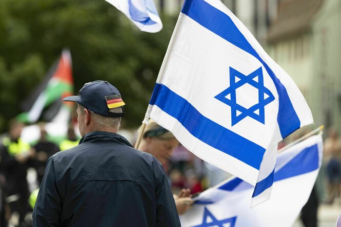 Ein Mann mit Deutschland-Flagge am Base-Cap und Israel-Flagge in der Hand