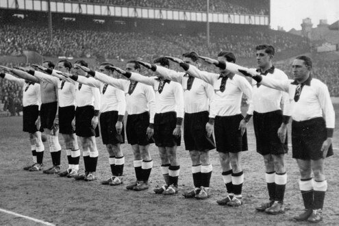 11 deutsche Fußballer zeigen vor Spielbeginn in einer Reihe den Hitlergruß