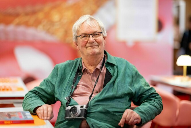 Porträt von Martin Parr, um seinen Hals hängt eine Kamera, er trägt eine grüne Jacke