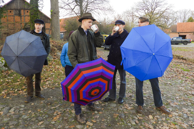 Junge Männer mit Regenschirmen trinken aus Bechern