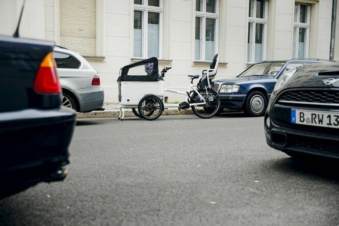 Ein Lastenrad parkt zwischen Autos am Straßenrand