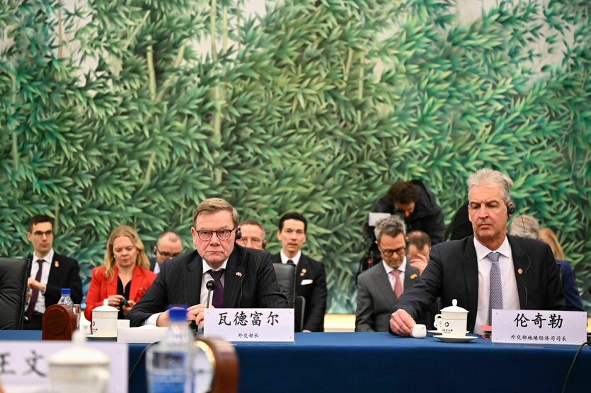Die deutsche Delegation sitzt an einem Tisch mit blaueer Decke, in der Reieh dahinter die Mitarbeitenden - Eine Fototapete zeigt Bambusblätter
