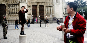 Touristen posieren vor Notre-Dame, ein Soldat schaut zu