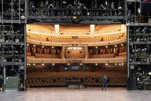 eine Person steht auf einer Theaterbühne und blickt in den Saal