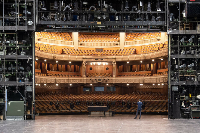 eine Person steht auf einer Theaterbühne und blickt in den Saal