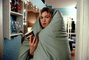 Eine Frau steht in eine Decke gewickelt in einer Wohnung und hält einen Becher Eiscreme