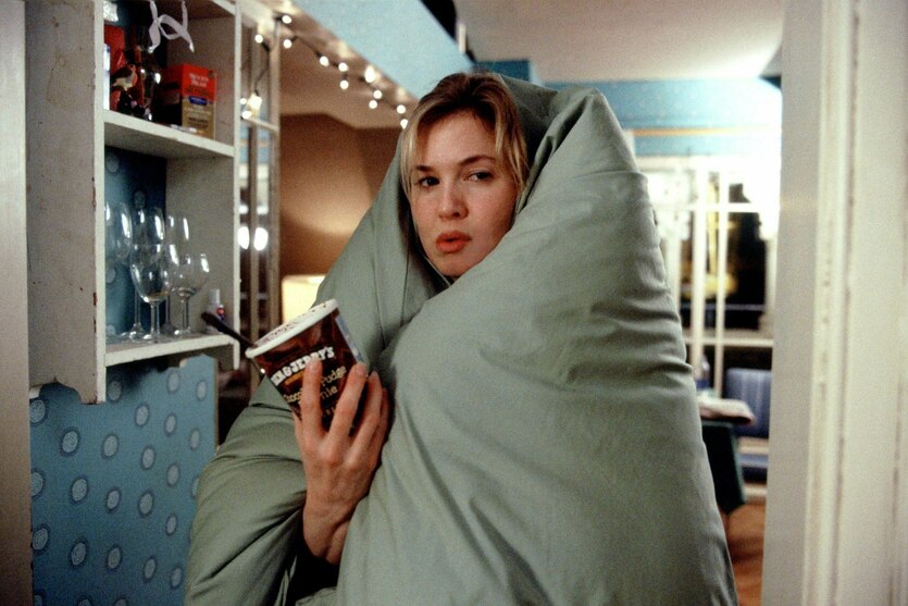 Eine Frau steht in eine Decke gewickelt in einer Wohnung und hält einen Becher Eiscreme